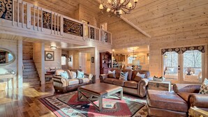 A spacious log cabin interior with a high ceiling, a staircase leading to a balcony, leather furniture, and a central rug. - Sunset Mountain Views- Spacious Luxurious cabin (Morganton)
