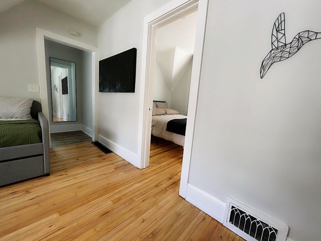 A room with a bed, a desk, and a chair. There is a door leading to another room.
