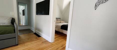 A room with a bed, a desk, and a chair. There is a door leading to another room.