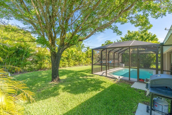 Un jardin avec une piscine, un patio couvert et un espace barbecue.
