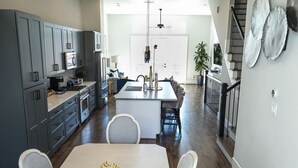 A modern kitchen with grey cabinets, a central island, and a dining area with a table and chairs. - Elegant Lux Townhome. 3BD, 3.5BTH. DOWNTOWN HTX (Houston)