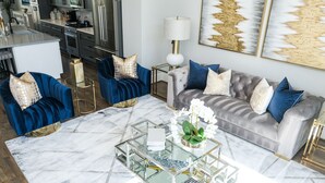 A modern living room with a grey sofa, blue armchairs, and a glass coffee table. - Elegant Lux Townhome. 3BD, 3.5BTH. DOWNTOWN HTX (Houston)