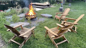 Ein Lagerfeuer mit Holzstühlen in einer grünen Wiese in der Nähe eines Teichs.