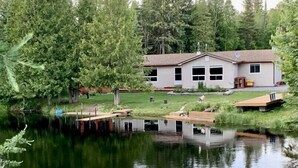 Ein Haus mit einem Steg, der in einen ruhigen Teich führt, umgeben von dichtem Baumbestand.