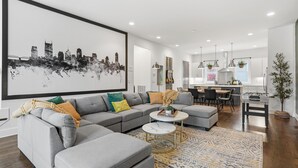 A modern living room with a grey sectional sofa, a marble coffee table, and a cityscape artwork on the wall. - Roof Top Deck with Skyline View - NO BUNKS - Pet and Kid Friendly (Nashville)