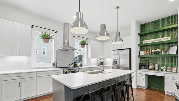 A modern kitchen with white cabinets, a large island with bar stools, hanging pendant lights, and a green accent wall with a sign. - Roof Top Deck with Skyline View - NO BUNKS - Pet and Kid Friendly (Nashville)