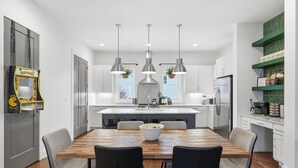 A modern kitchen with a central island, pendant lights, and a dining area with a wooden table and chairs. - Roof Top Deck with Skyline View - NO BUNKS - Pet and Kid Friendly (Nashville)