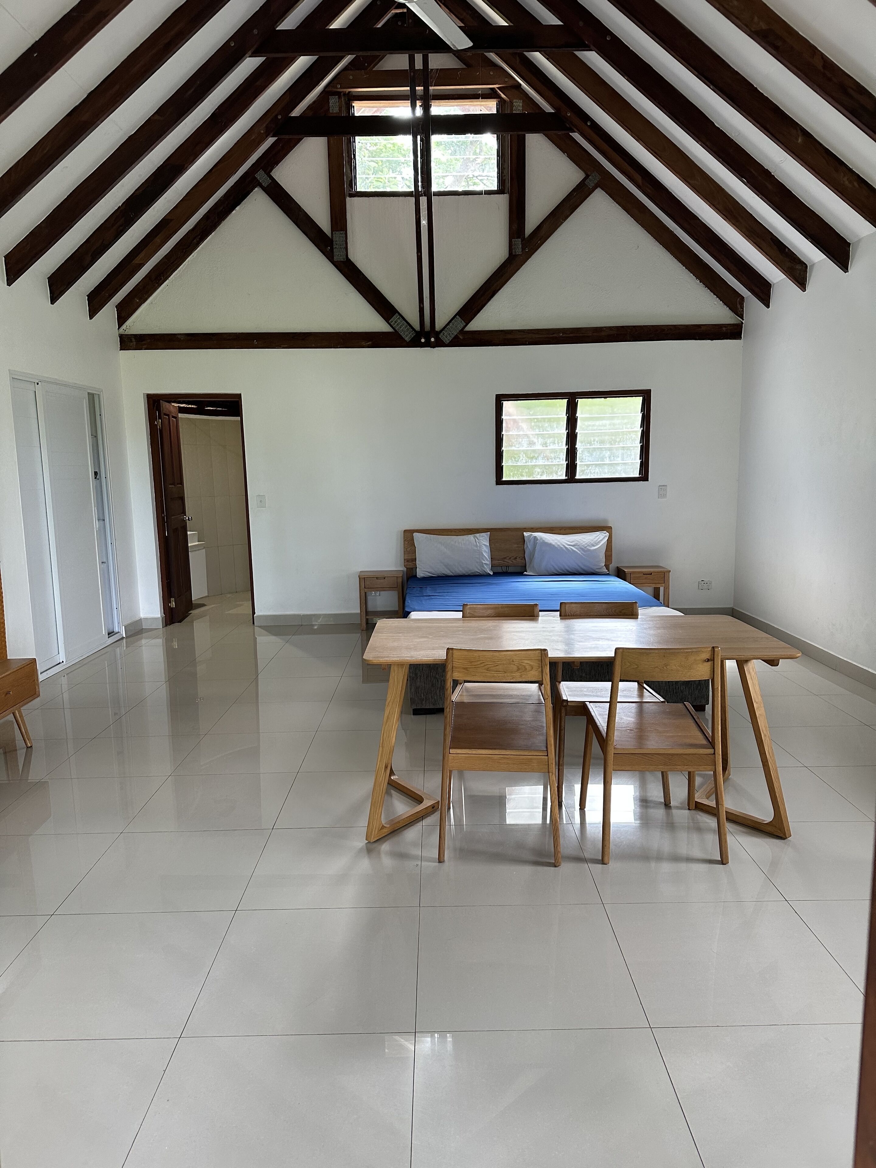 Une pièce spacieuse avec un plafond haut, une table à manger en bois avec des chaises, un canapé et une fenêtre avec des stores.