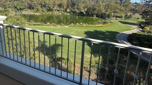Vista de uma varanda com vista para um campo de golfe, um lago, árvores e um céu azul claro.