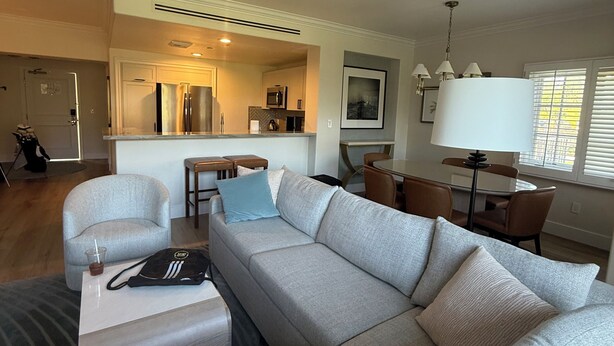 Uma sala de estar moderna com um sofá seccional grande, um espaço de refeições com mesa e cadeiras, e uma cozinha ao fundo.
