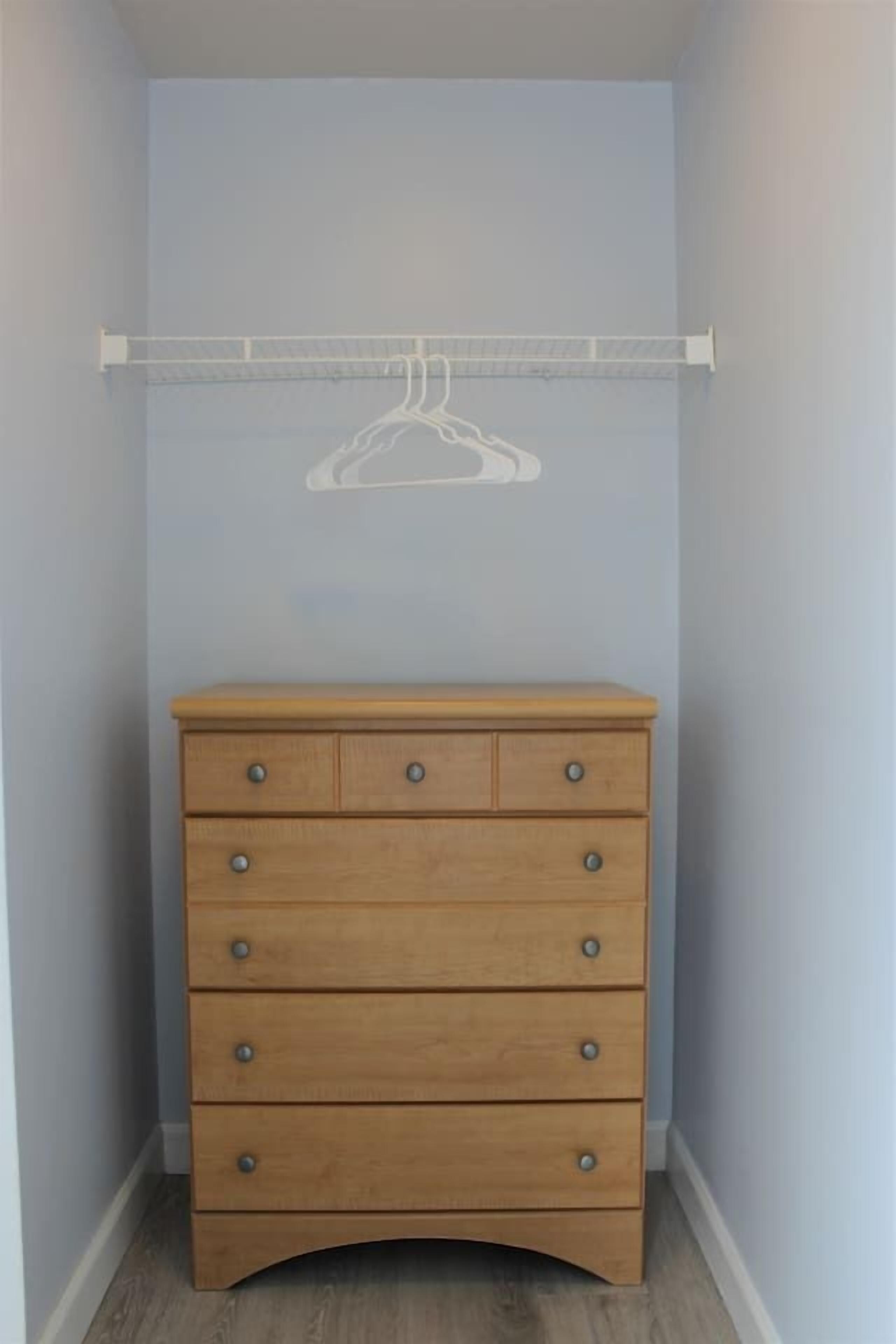 A corner room with a wooden dresser, a white closet rod, and a light blue wall.