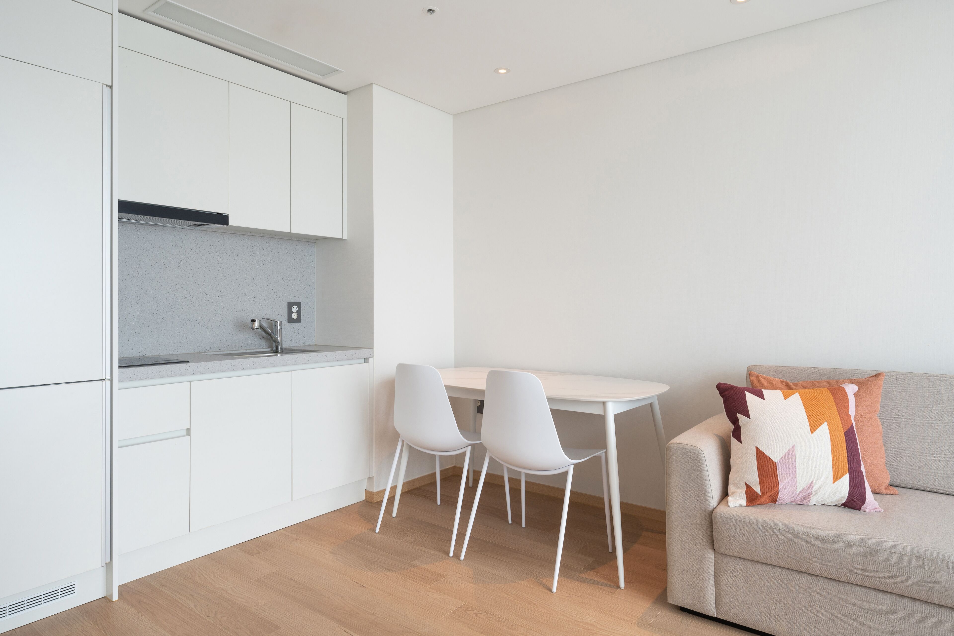 Una cocina moderna con armarios blancos, encimera gris y dos sillas blancas.