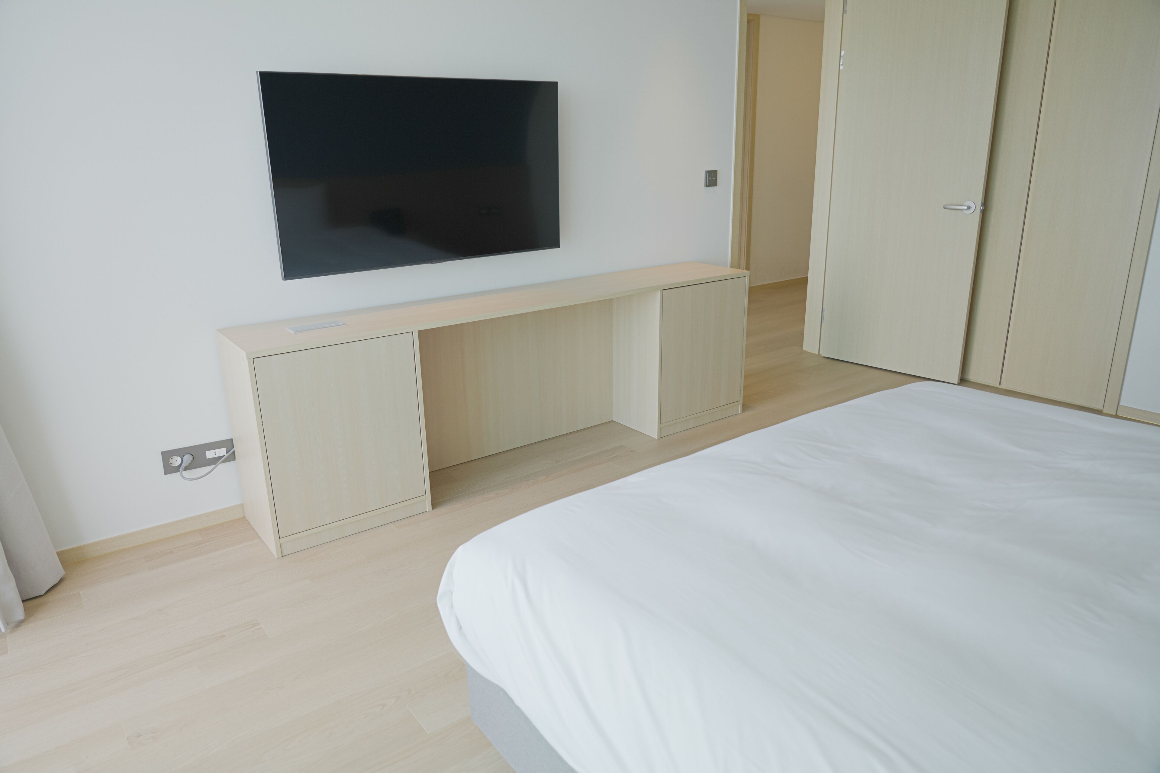 Un dormitorio con cama, televisión montada en la pared, escritorio y armario.
