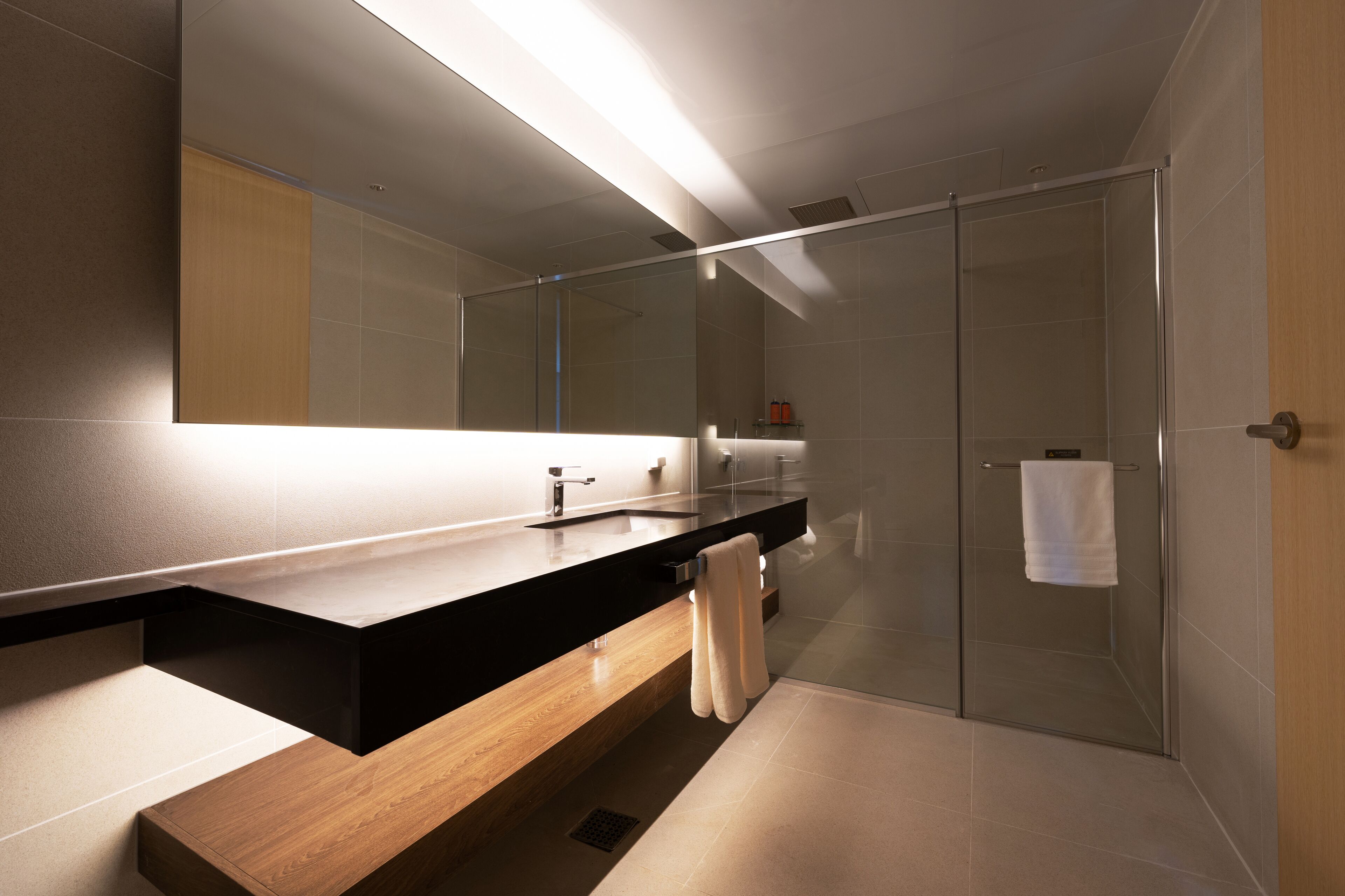 Un baño moderno con tocador de madera, cabina de ducha de vidrio y un espejo grande.