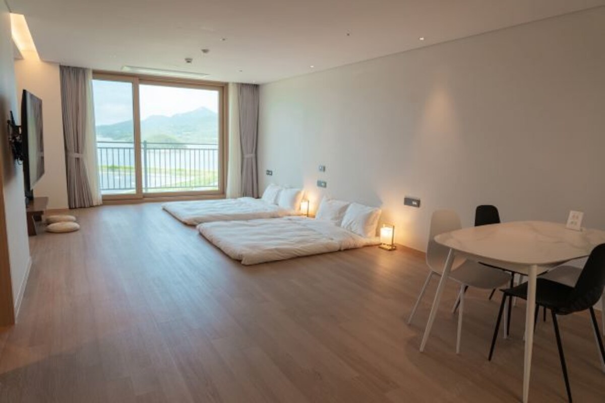 A modern hotel room with a large bed, a dining table, and a balcony with a view of the mountains.