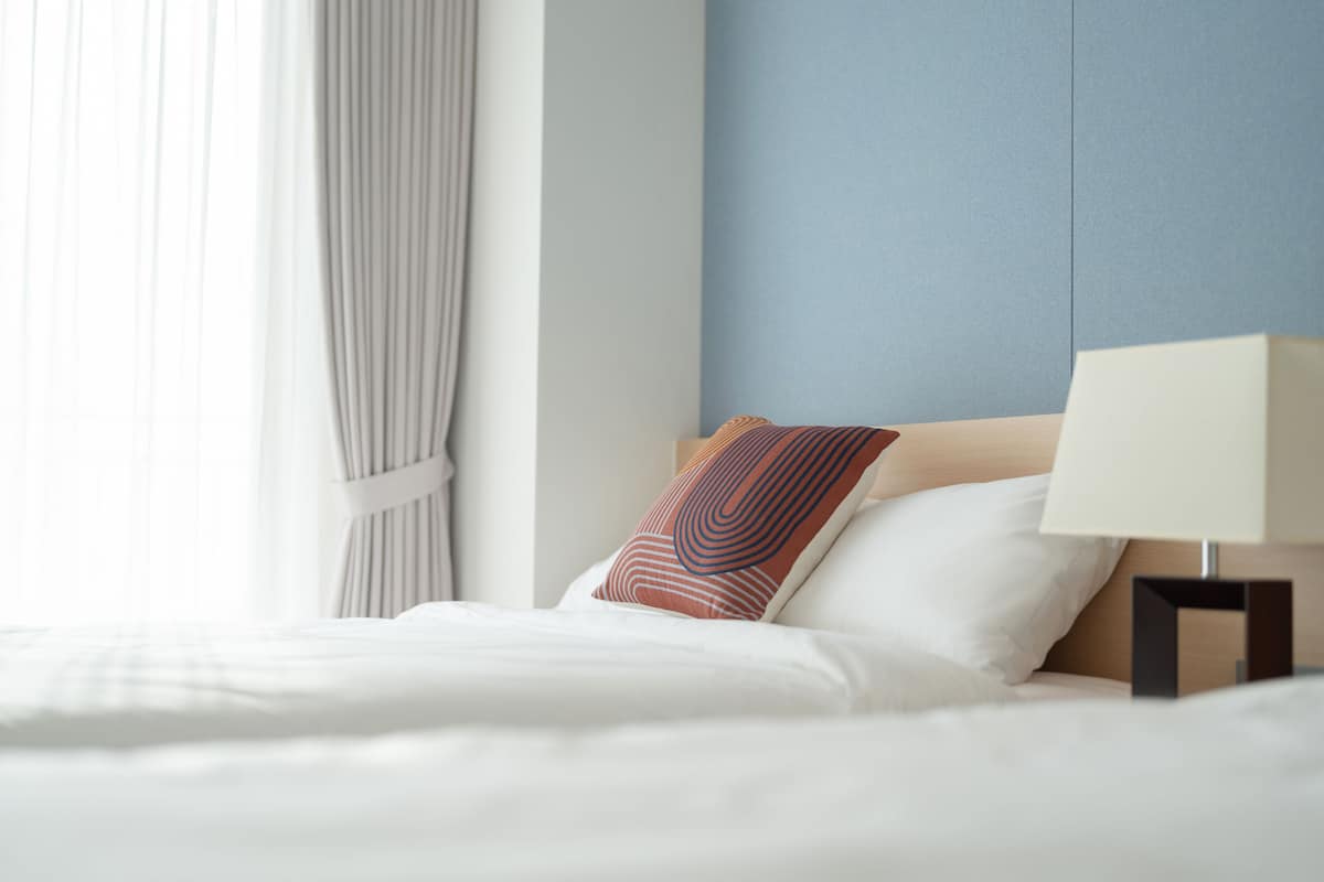 A neatly made bed with white linens, a wooden headboard, and a single decorative pillow.