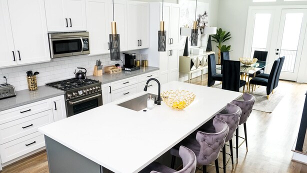 Une cuisine moderne avec des meubles blancs, un îlot central doté de tabourets de bar et un coin repas avec une table et des chaises noires.