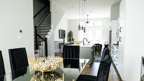 Une cuisine moderne avec des meubles blancs, un îlot central et un coin repas comprenant une table en verre et des chaises noires.