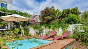 Um deck de madeira com piscina, cadeiras de descanso e um guarda-sol.