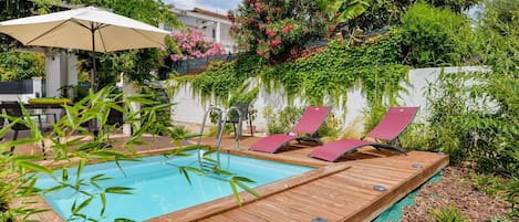 Um deck de madeira com piscina, cadeiras de descanso e um guarda-sol.