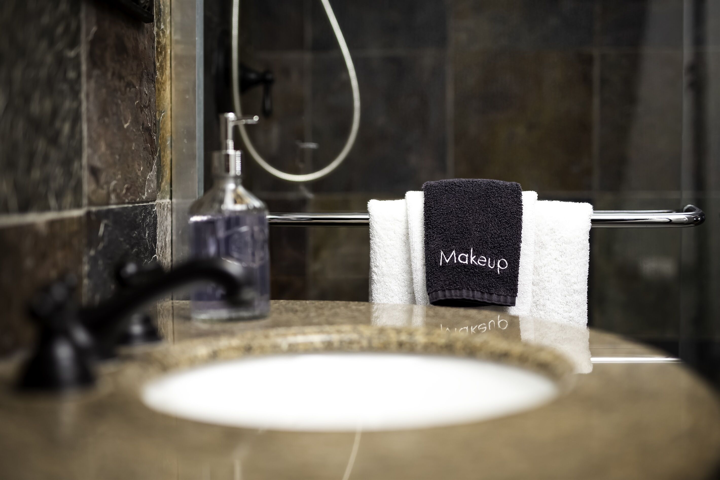 A bathroom with a marble sink, a towel rack with a black towel labeled "Makeup," and a handheld showerhead.