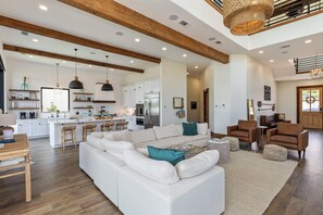 Ein geräumiges Wohnzimmer mit einem großen weißen Ecksofa, einem Holzessttisch und einer Küche im Hintergrund.