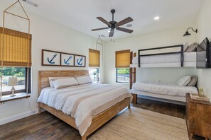 A bedroom with a wooden bed, a bunk bed, a ceiling fan, and windows with blinds.