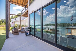 A modern outdoor patio with a grill, seating, and a view of a lake.