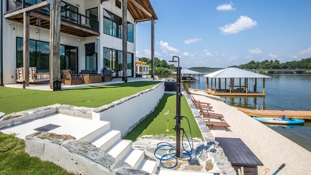 A modern house with a deck, a pool, and a gazebo by the water.