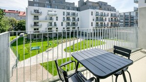 A balcony with a table and chairs, overlooking a courtyard with a green lawn and a playground. - Amazing Landstraße 2BR w/ Elevator & Playglound, Calm Area, by Blueground (Vienna)