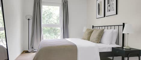 A bedroom with a bed, bedside table, lamp, and curtains.