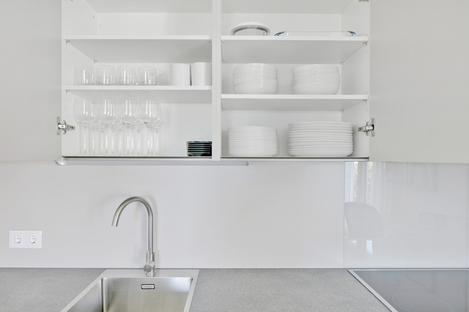 Une cuisine moderne dotée d’un évier en acier inoxydable, de meubles blancs et de présentoirs à verres.