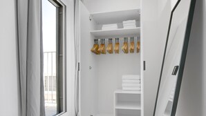 En rymlig klädkammare med plats för att hänga kläder och hyllor, ett fönster med gardiner och ett trägolv.