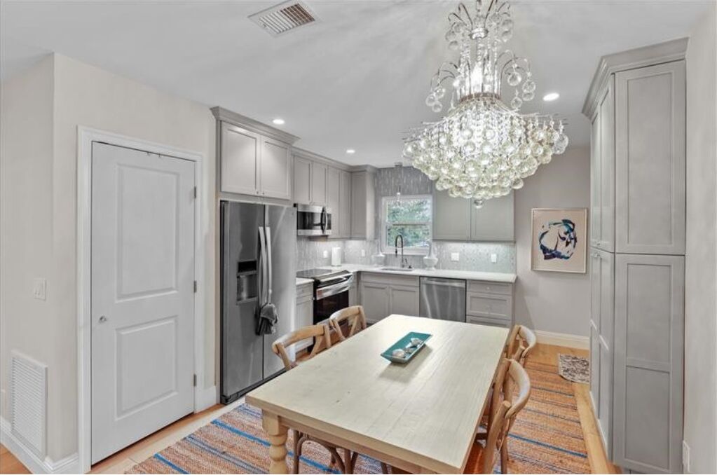 A modern kitchen with white cabinetry, stainless steel appliances, and a chandelier.
