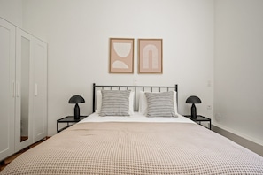 A bedroom with a bed, two bedside tables, a wardrobe, and two framed pictures on the wall.