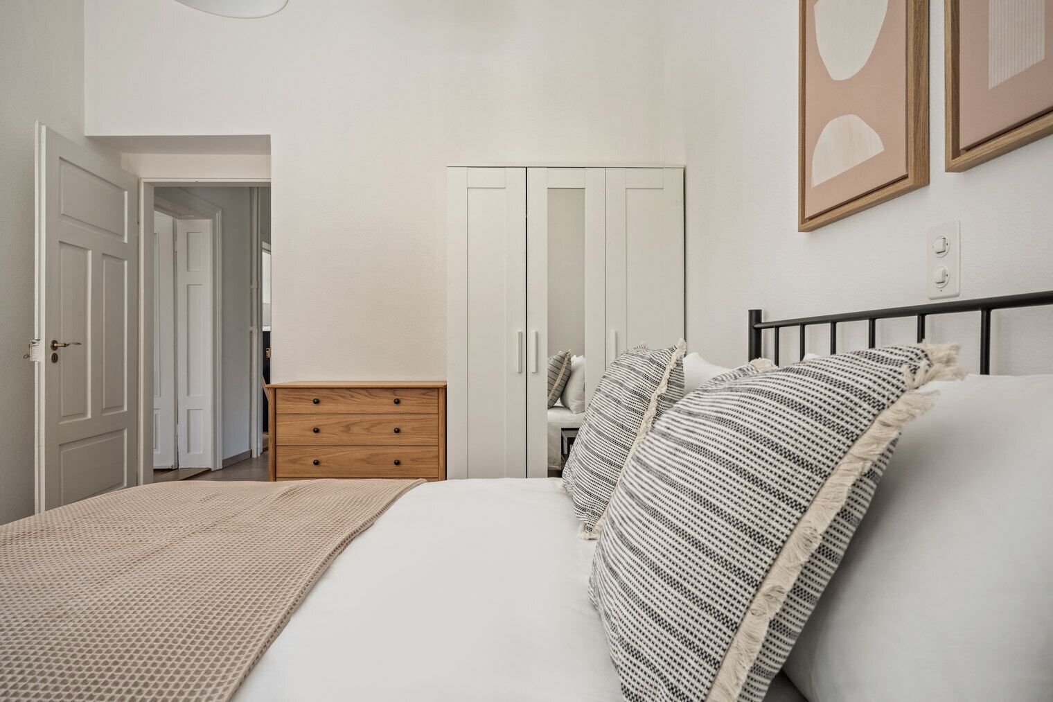 Een slaapkamer met een bed, een houten dressoir, een kledingkast en een deur naar een andere kamer.