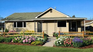 Ein eingeschossiges Haus mit Veranda, Garage und einem kleinen Garten mit verschiedenen Blumen.