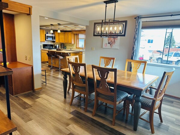 A dining area with wooden chairs and a table, a kitchen with wooden cabinets, and a large window.