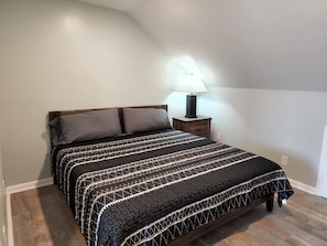 A bedroom with a bed, two pillows, a bedside table with a lamp, and a wooden floor. - Harrison Hotel Unit I
Pet Friendly
2nd Story (Murrells Inlet)