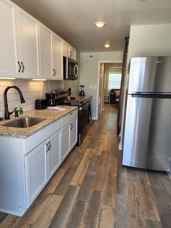 A kitchen with white cabinets, a granite countertop, a stainless steel refrigerator, and a wooden floor. - Harrison Hotel Unit I
Pet Friendly
2nd Story (Murrells Inlet)