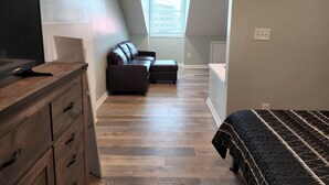 Een kamer met een houten dressoir, een leren bank, een bed met een bedovertrek met patroon, en een raam met uitzicht op de stad.