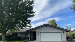 A single-story house with a garage, a well-maintained lawn, and a large tree in the foreground. - Arroyo Manor - Centrally Located (Redding)