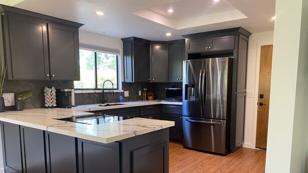 A modern kitchen with dark cabinets, a stainless steel refrigerator, and a large island. - Arroyo Manor - Centrally Located (Redding)