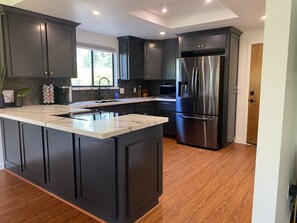 A modern kitchen with dark cabinets, a stainless steel refrigerator, and a large island. - Arroyo Manor - Centrally Located (Redding)