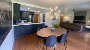 A modern kitchen with dark cabinetry, a central island, and a dining area with a round table and chairs. - Arroyo Manor - Centrally Located (Redding)