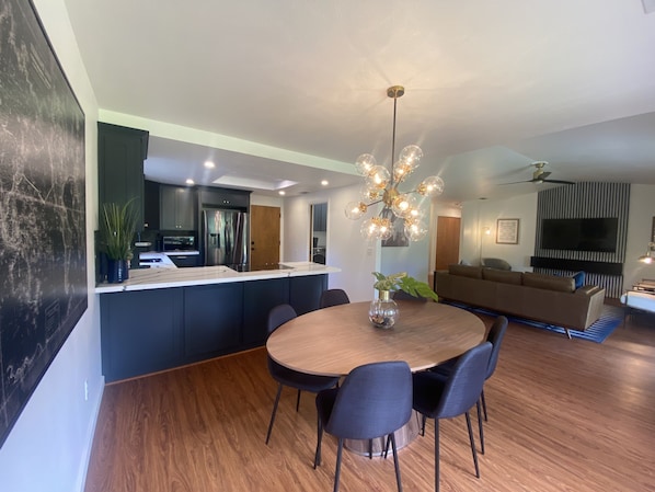 Une cuisine moderne avec des meubles de couleur sombre, un îlot central et un coin repas comprenant une table ronde et des chaises.