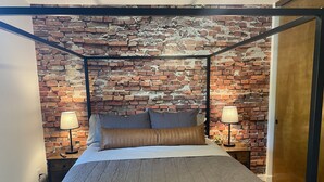 A bedroom with a brick wall, a four-poster bed, and two bedside lamps. - Arroyo Manor - Centrally Located (Redding)