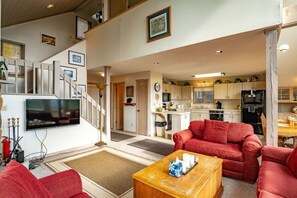 A spacious living area with a red sofa, a coffee table, and a television. A staircase leads to an upper level.