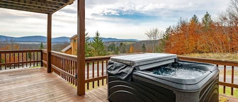 A hot tub on a wooden deck with a view of mountains and autumn trees.