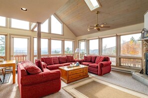 A spacious room with a high ceiling, large windows, a ceiling fan, and a fireplace.